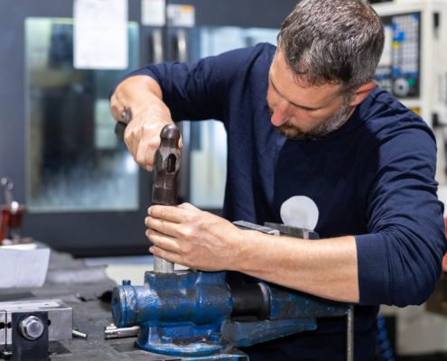 Professional worker working on a steel piece with hammer in a metal factory workshop